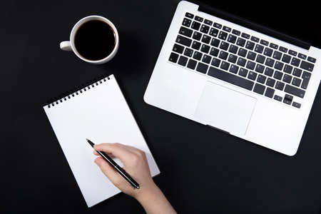hand holds pen over notebook on black table near laptop.の写真素材