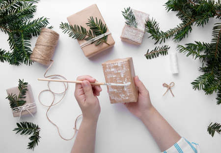 Hands hold one Christmas present and decorate it with white paint on desktop