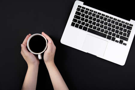 hands hold a cup of coffee on working black table next to laptopの写真素材