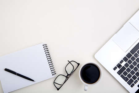 light office desk with laptop, white notebook mockup, glasses and coffee cup.の写真素材