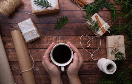 Hands hold a cup of coffee on the table on which there are Christmas giftsの写真素材