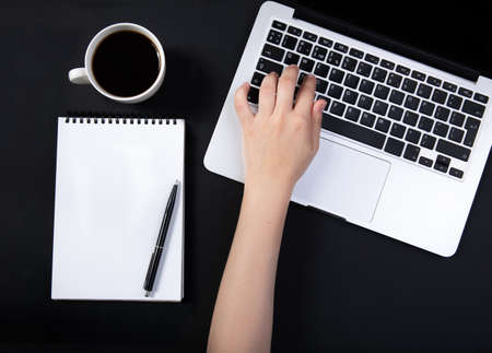 Black office desk with laptop, white mockup notebook, pen and cup of coffee.の写真素材