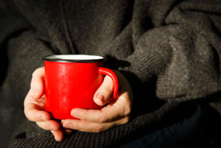 red metal mug in the hands of a girl in a gray sweaterの写真素材