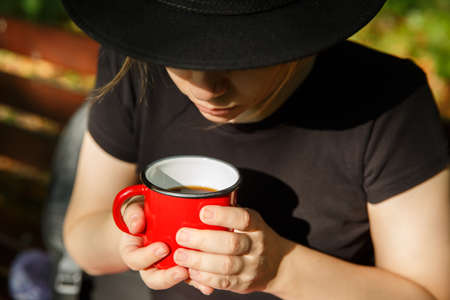 girl in hat holding red metal mug in her hands with drinkの写真素材