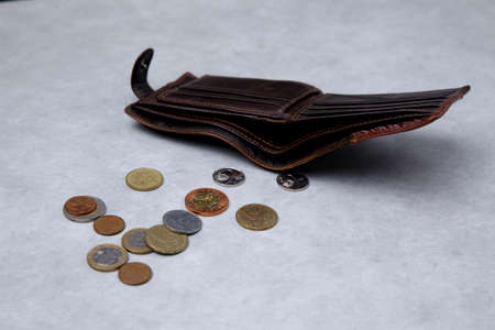 leather wallet from which small coins are poured onto a light tableの写真素材