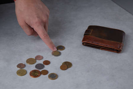 A mans hand counting metal coins and a leather wallet lies nearbyの写真素材