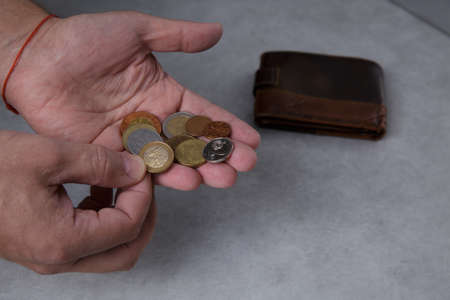 Hands of a man who are counting metal coins on the palm and a leather walletの写真素材
