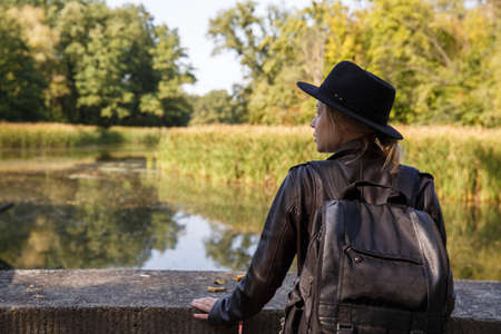 a young Caucasian woman in a leather jacket and hat stands by the pondの写真素材
