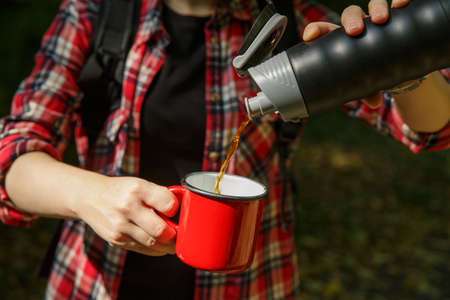 tourist hands pour coffee from a into a metal red cupの写真素材