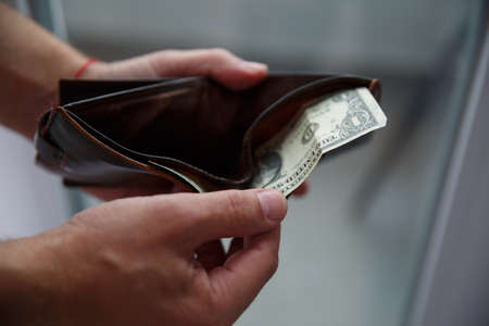 Mans hands pull out a dollar bill from a leather wallet