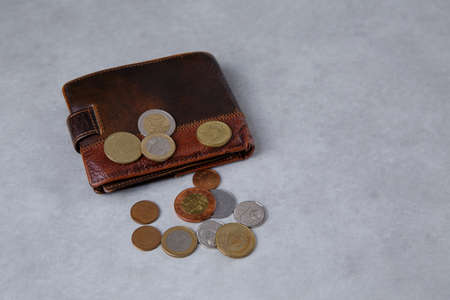 an old wallet lies on a light table and there are small metal coins on itの写真素材