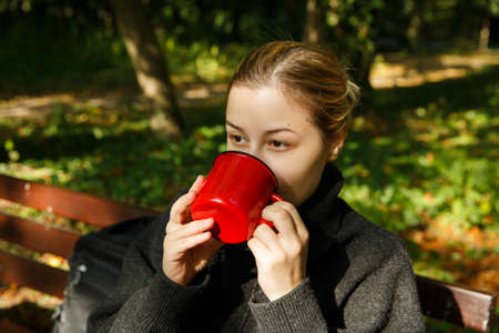 caucasian woman in a warm sweater holds red mug in her hands.の写真素材