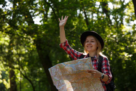 young caucasian woman in a hat with a map waving in greeting.