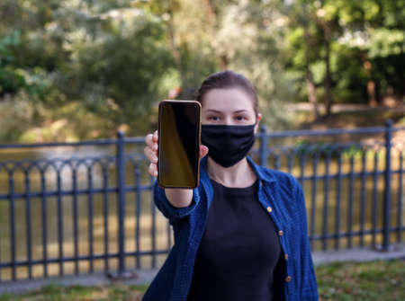 Girl in a black protective mask holds a phoneの写真素材