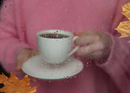 white cup in hand and window with raindrops.background blurred. selective focus.の写真素材