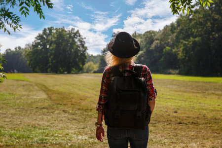 young caucasian woman with a backpack and hat near the field.の写真素材