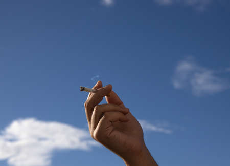cigarette in a man hand against a blue sky. close up.の写真素材
