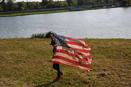 a young girl holding a scarf with a pattern of American flag waving in the windの写真素材