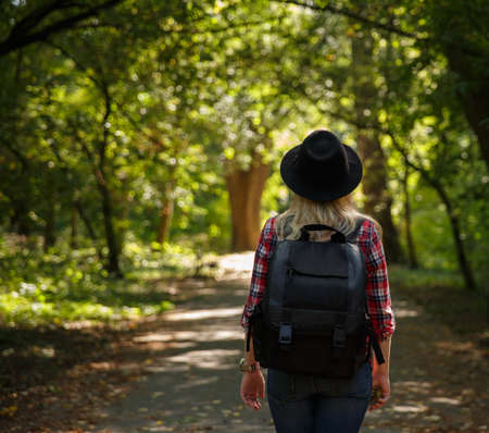 young caucasian girl travels in a hat and with a backpack through the forestの写真素材