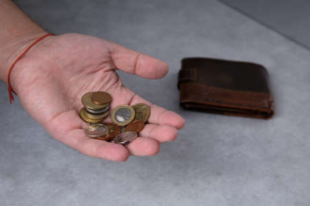 A man in his palm holds metal coins and a leather wallet lies nearbyの写真素材