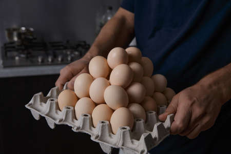 a man holding a full tray of chicken eggs in his own kitchenの写真素材