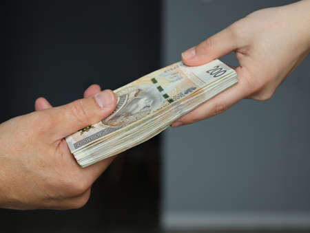 male hand giving a bundle of large banknotes to female handsの写真素材