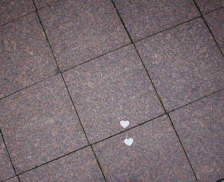 two white paper hearts lie on the sidewalk granite tilesの写真素材