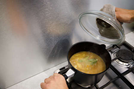 hands hold a pot with potatoes and meat that stands on the stove