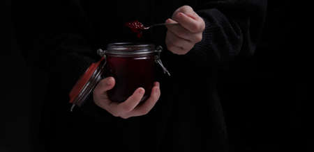 hands hold a jar of strawberry jam and a spoon on a dark backgroundの写真素材