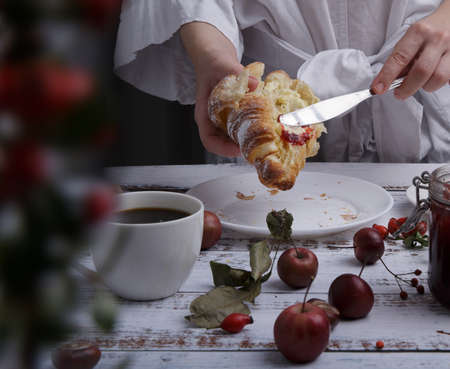 hands hold a croissant and use a knife to spread strawberry jam on itの写真素材