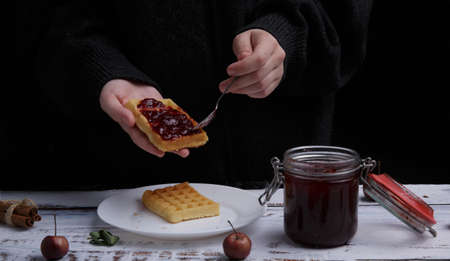 child hands spread strawberry jam with a spoon on Belgian waffles.の写真素材