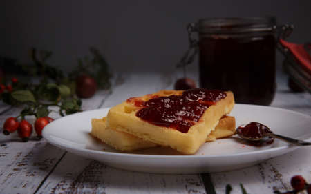 soft waffles smeared with strawberry jam and a glass jar with jam.の写真素材