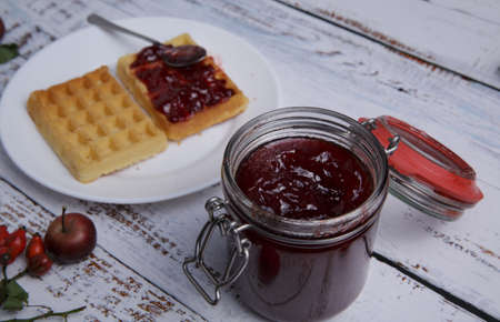jar of strawberry jam and a plate of Belgian waffles on a white tableの写真素材