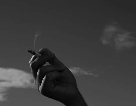 cigarette in a man hand against a blue sky. close up.の写真素材