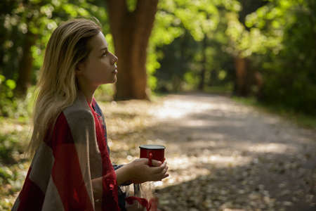young caucasian woman drinking from red metal mug in natureの写真素材