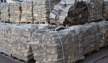 neatly chopped firewood for the fireplace is packed on pallets packed in netsの写真素材