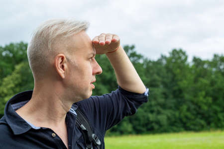 the gray-haired man, closing his eyes with his hand from the sun, looksの写真素材