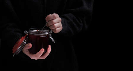 hands hold a jar of strawberry jam and a spoon on a dark background.の写真素材