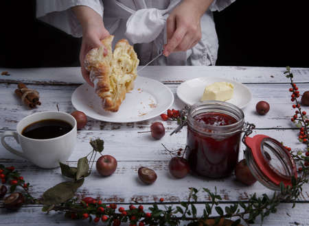 hands hold a croissant and use a knife to spread butterの写真素材