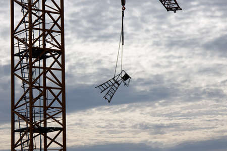 The crane moves the stepladder against the sky with cloudsの写真素材