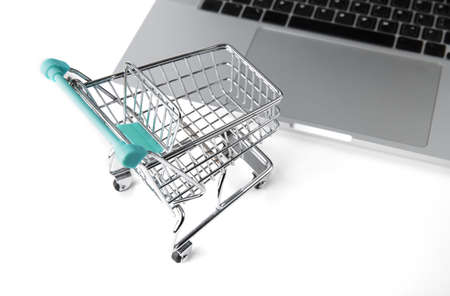 miniature shopping cart from a store stands next to a laptop