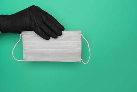 hand in black latex glove holds medical mask on green background. High quality photoの写真素材