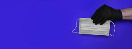 hand in a black latex glove holds a medical mask on a blue background. High quality photo