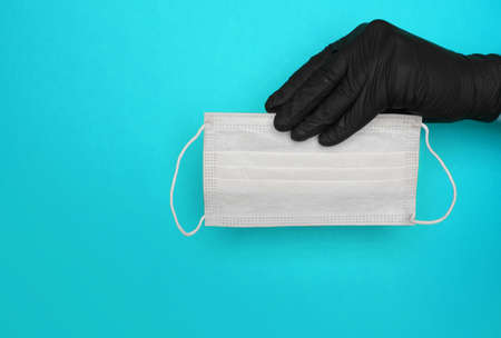hand in black latex glove holds medical mask on blue background. High quality photoの写真素材