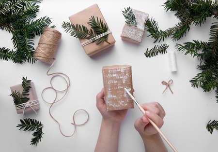Hands are holding one Christmas present and decorate the present with white paint on desktop with Christmas tree. Christmas packaging. Christmas mood. Happy boxing day.の写真素材