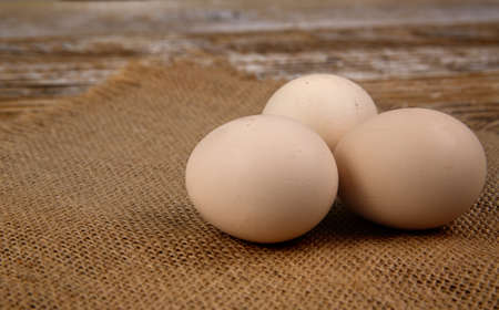 three fresh chicken eggs lie on burlap on rustic wooden table. selective focusの写真素材
