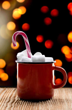 cup of cocoa with marshmallows stands on wooden table the background of garlands and candy cane in cup. High quality photoの写真素材