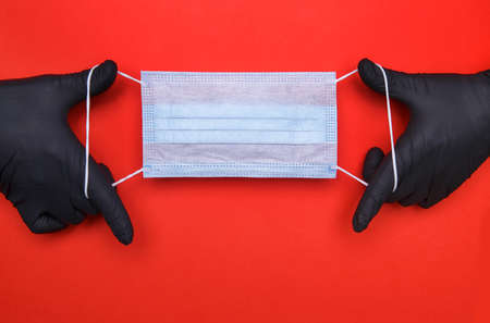 hand in a black latex glove holds a medical mask on a red background. High quality photoの写真素材