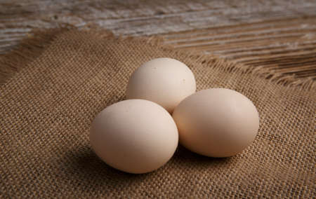 three fresh chicken eggs lie on burlap on rustic wooden table. selective focus .の写真素材