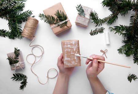 Hands are holding one Christmas present and decorate the present with white paint on desktop with Christmas tree. Christmas packaging. Christmas mood. Happy boxing day.の写真素材